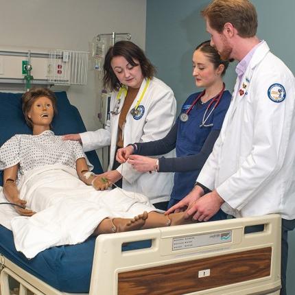 Three U N E students from different health majors work together on a dummy in the 仿真实验室